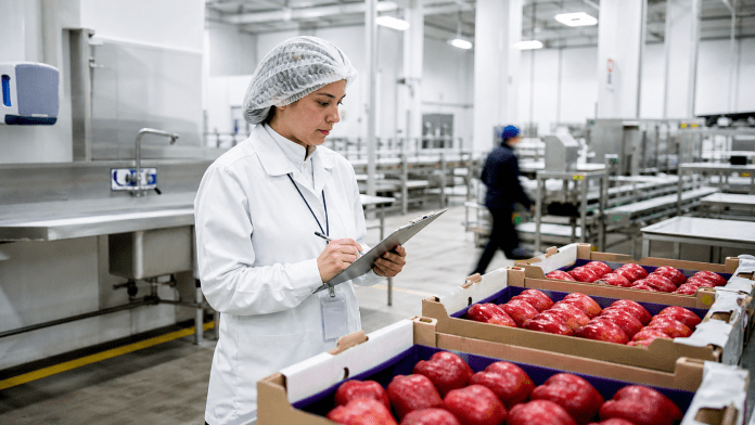Auditora revisando una operación de packing de manzanas con controles documentados.