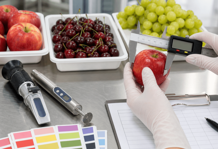 Mesa de control de calidad con frutas, calibre digital, colorímetro y planilla de inspección.