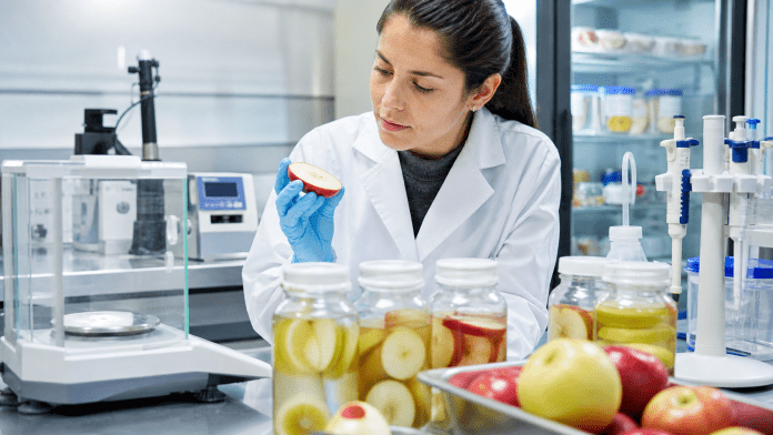 Técnica de laboratorio analizando una manzana junto a instrumentos de control de calidad.