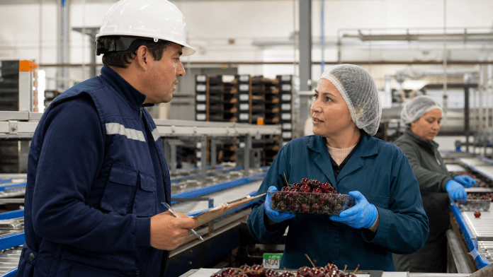 Supervisor de calidad conversando con un operador junto a una línea de packing de fruta.